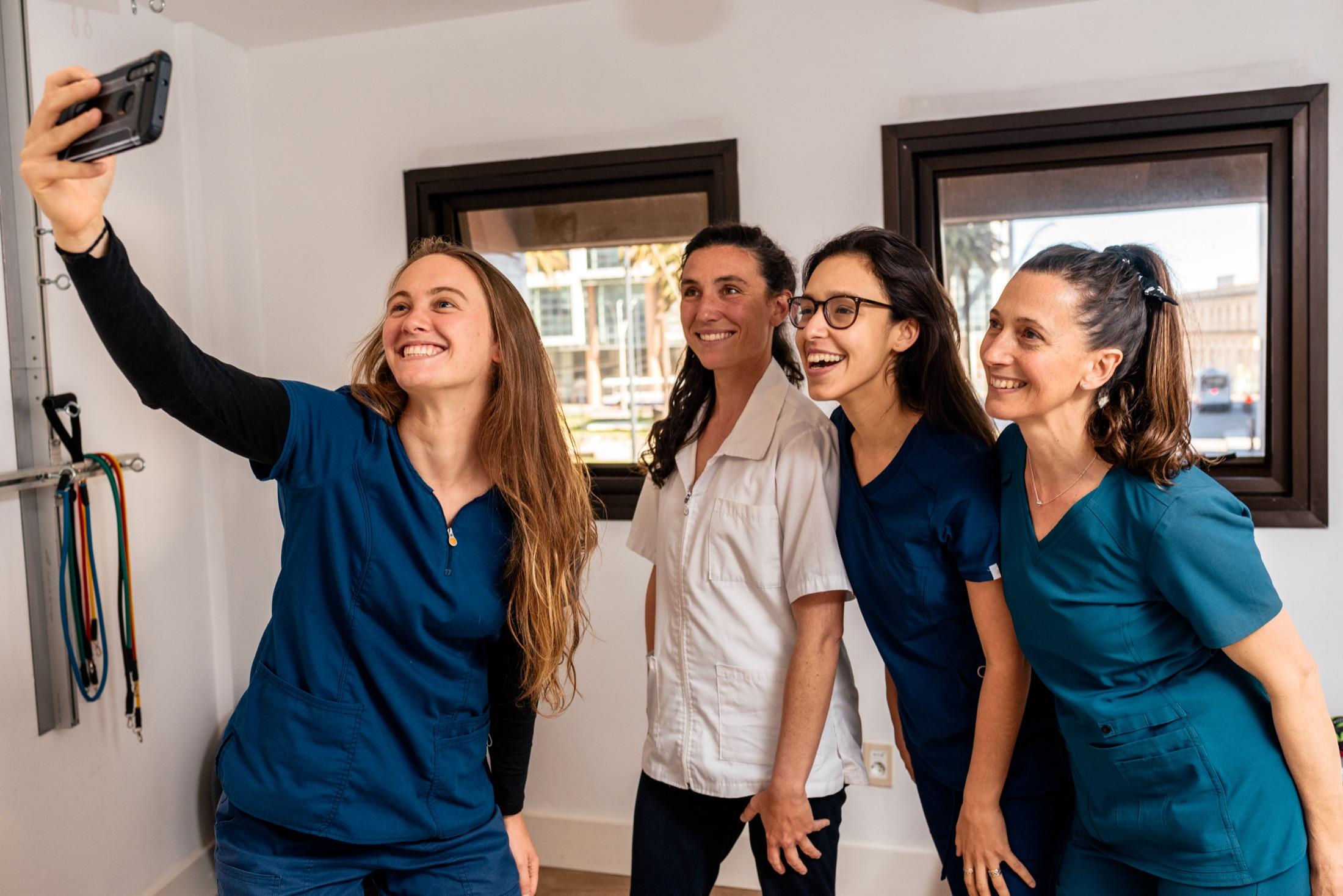 Four smiling clinicians in scrubs taking a group selfie together